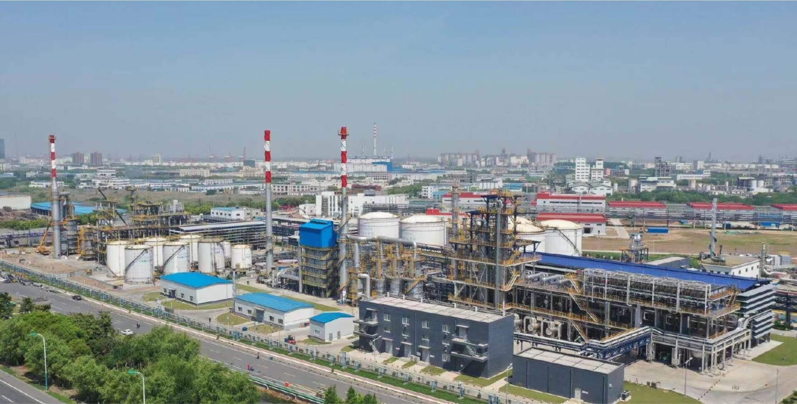 Aerial view of the EcoCeres HVO plant: storage tanks, process columns and red-and-white stacks on an industrial site beside a highway